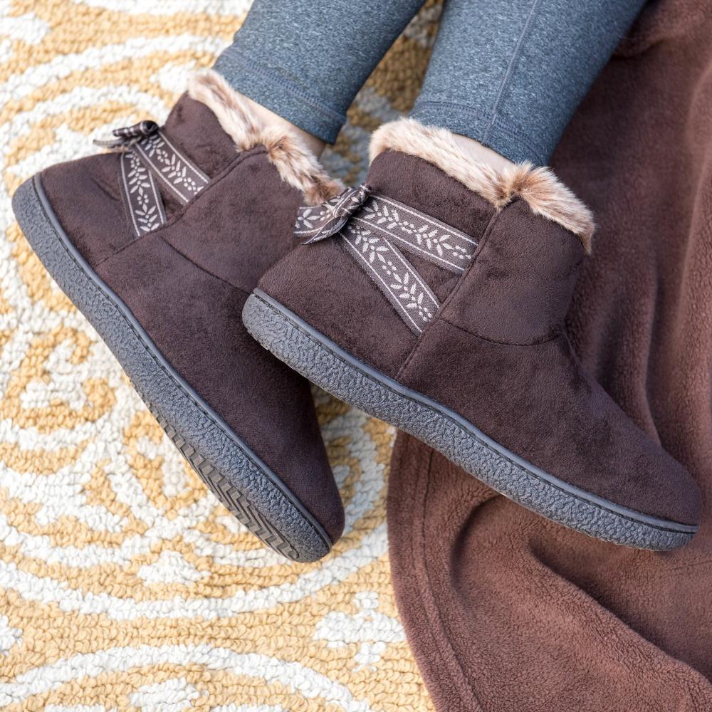 Women's Microsuede Addie Boot Slippers with Bow in Dark Chocolate on Model laying on rug and brown blanket showing off the bow-ribbon detailing