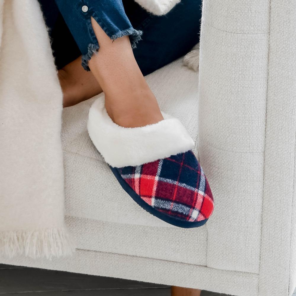 Women's Plaid Page Hoodback Slippers in Navy Blue on Figure. Model is sitting in a comfy chair with her feet up on the edge