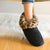 Women's Microsuede Noela Boot Slippers in Black with Cheetah Print Cuff on figure sitting on a chair with a fluffy rug behind the chair