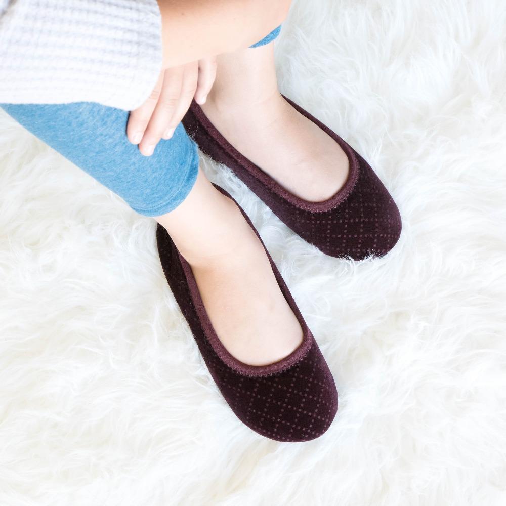 Women's Memory Foam Velour Sabrine Ballerina Slippers in Henna Maroon on model sitting on a fluffy rug with her arms hugging her knees