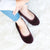 Women's Memory Foam Velour Sabrine Ballerina Slippers in Henna Maroon on model sitting on a fluffy rug with her arms hugging her knees