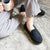 Men's Microterry and Waffle Travis Moccasin Slippers in Black on figure model sitting on cozy blanket in loungewear with a cup of coffee